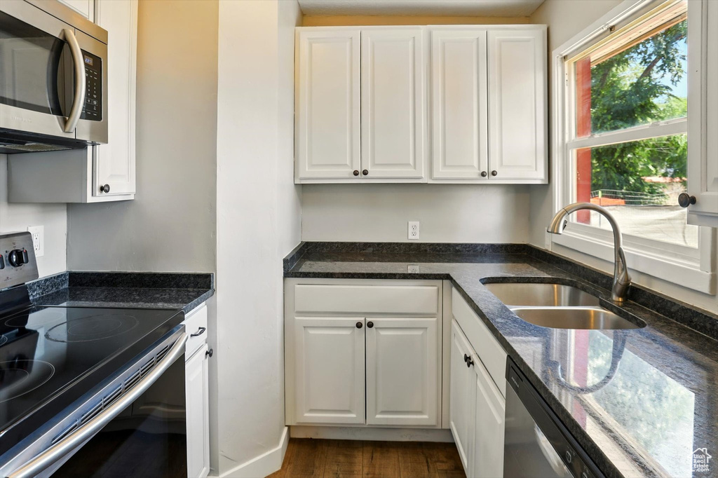 Kitchen with appliances with stainless steel finishes, white cabinetry, and dark stone counters