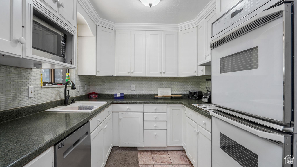 Kitchen featuring dishwasher, double oven, white cabinetry, decorative backsplash, and dark countertops