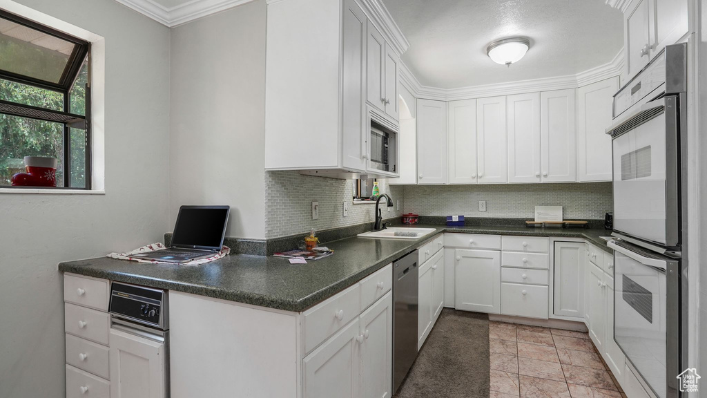 Kitchen featuring stainless steel appliances, decorative backsplash, white cabinetry, dark countertops, and ornamental molding