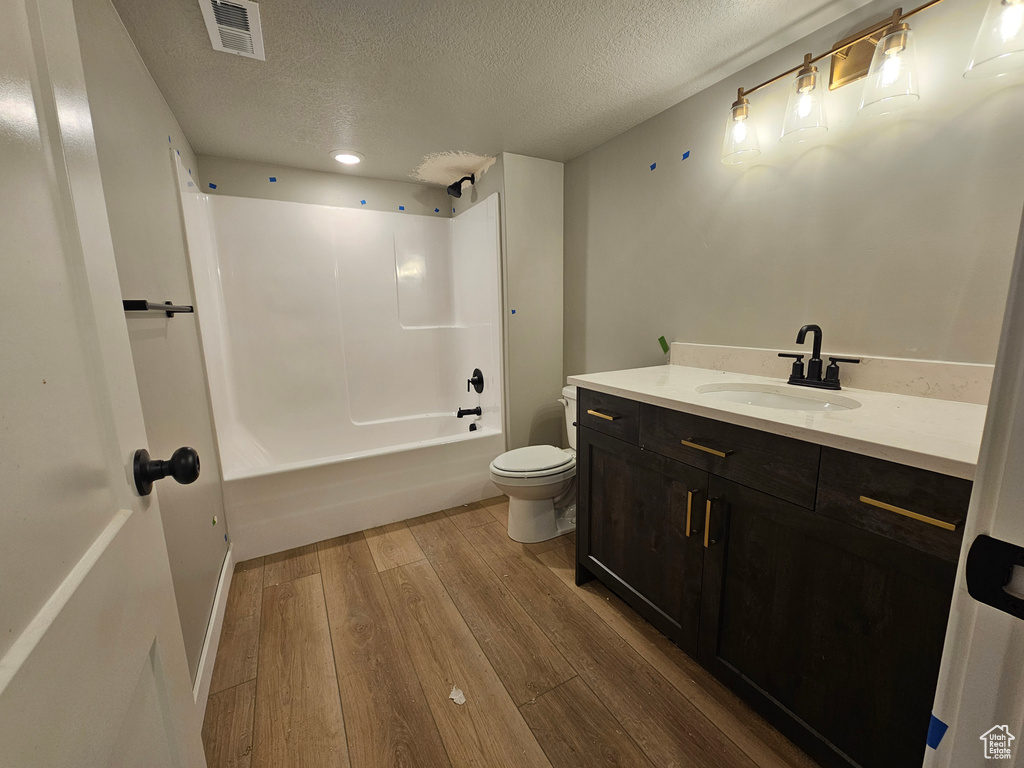 Full bathroom with vanity, a textured ceiling, wood finished floors, and shower / washtub combination