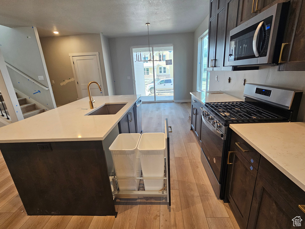 Kitchen with appliances with stainless steel finishes, light wood-style floors, light countertops, a center island with sink, and recessed lighting