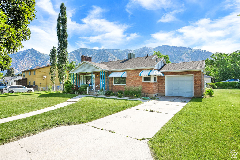 Single story home with a mountain view, concrete driveway, brick siding, an attached garage, and a chimney