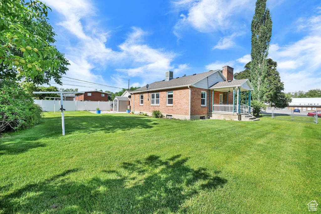 Back of property with brick siding, covered porch, a shed, and a fenced backyard