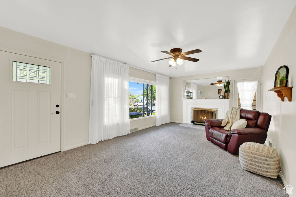 Living area featuring a ceiling fan, a lit fireplace, and carpet