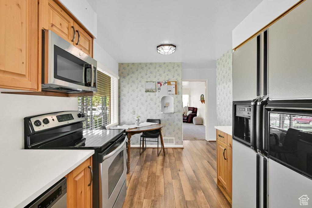 Kitchen featuring appliances with stainless steel finishes, wallpapered walls, wood-type flooring, and light countertops