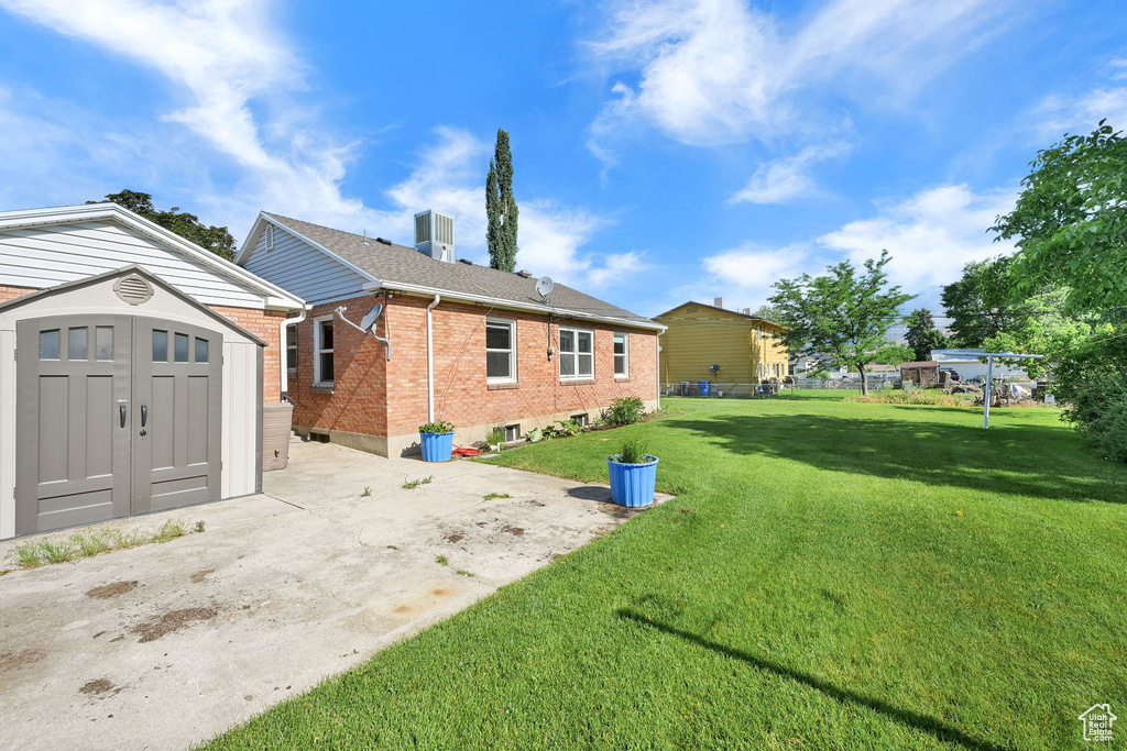 Back of house with a storage unit, brick siding, and a yard