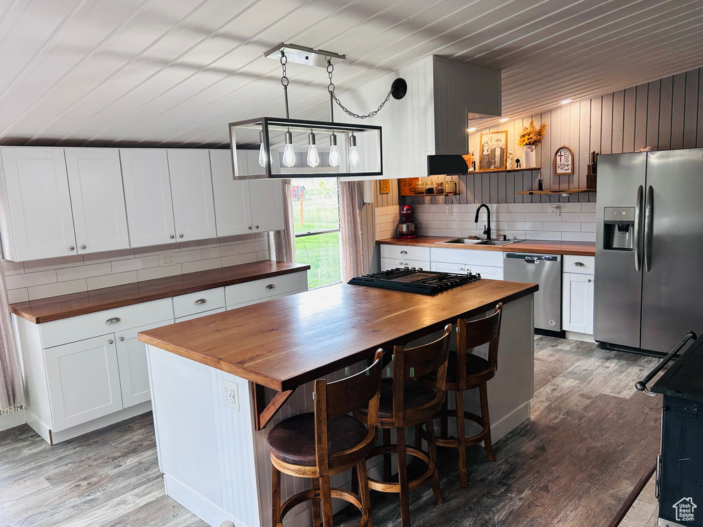 Kitchen with appliances with stainless steel finishes, butcher block counters, light wood-style floors, backsplash, and wood ceiling