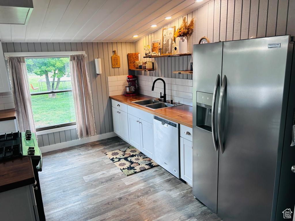 Kitchen with appliances with stainless steel finishes, wooden counters, open shelves, light wood-style floors, and wooden walls