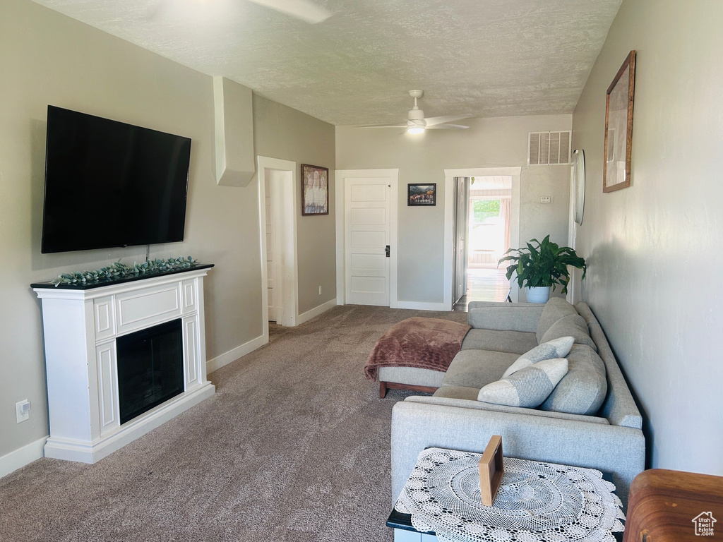 Living room featuring light carpet, a ceiling fan, a textured ceiling, and a fireplace