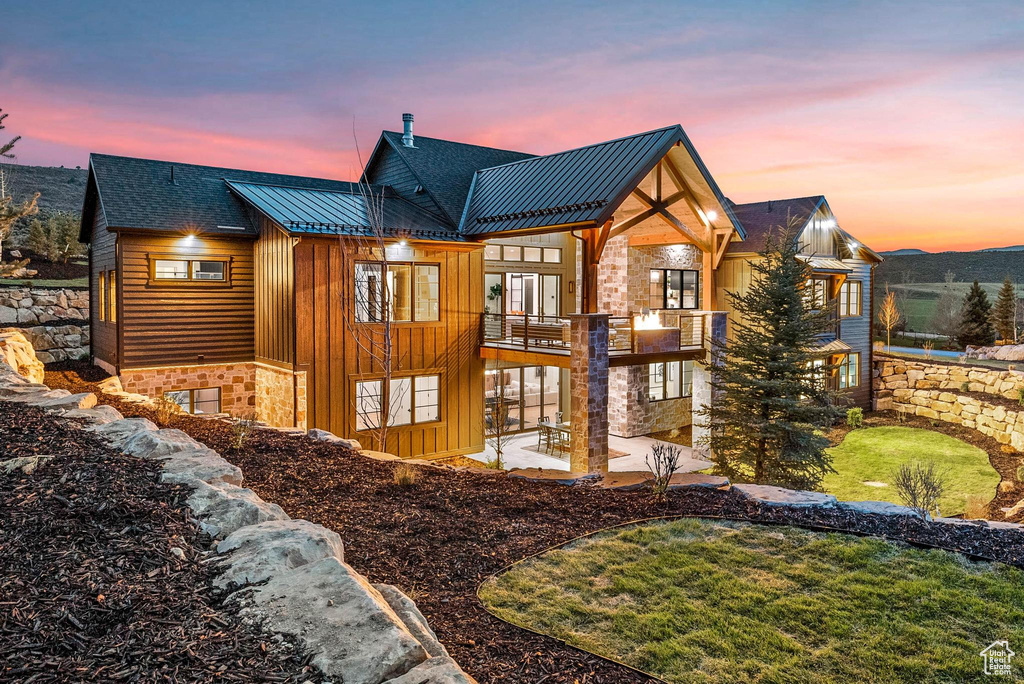 Back of house featuring board and batten siding, a patio, stone siding, a balcony, and a standing seam roof