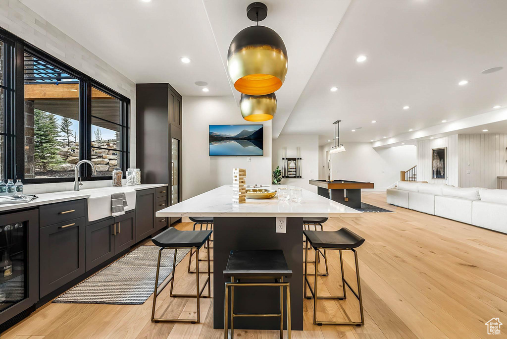 Kitchen featuring beverage cooler, light wood finished floors, a kitchen bar, open floor plan, and recessed lighting