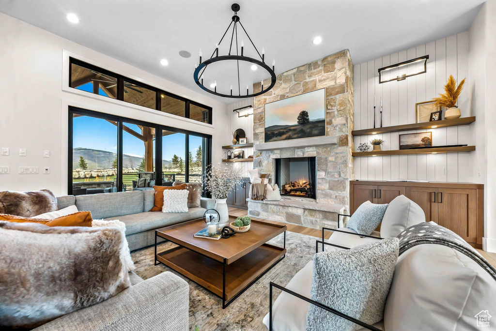 Living area with wood finished floors, a chandelier, recessed lighting, and a stone fireplace