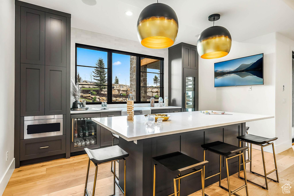 Kitchen featuring wine cooler, light countertops, light wood-style floors, and a kitchen bar