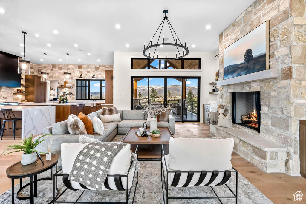 Living area with light wood finished floors, a stone fireplace, a chandelier, and recessed lighting