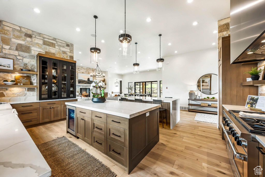 Kitchen with wall chimney exhaust hood, open shelves, a spacious island, light wood-style floors, and beverage cooler