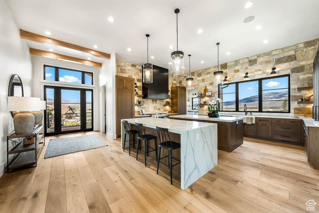 Kitchen with a spacious island, exhaust hood, recessed lighting, light wood-style flooring, and a kitchen breakfast bar