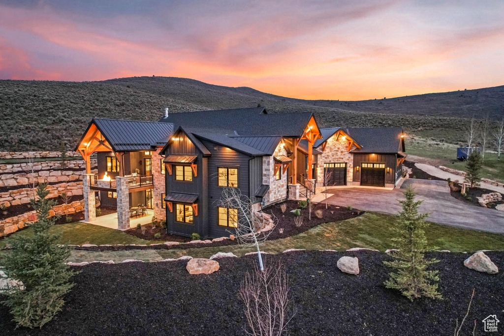 View of front facade featuring a standing seam roof, stone siding, a garage, board and batten siding, and a balcony