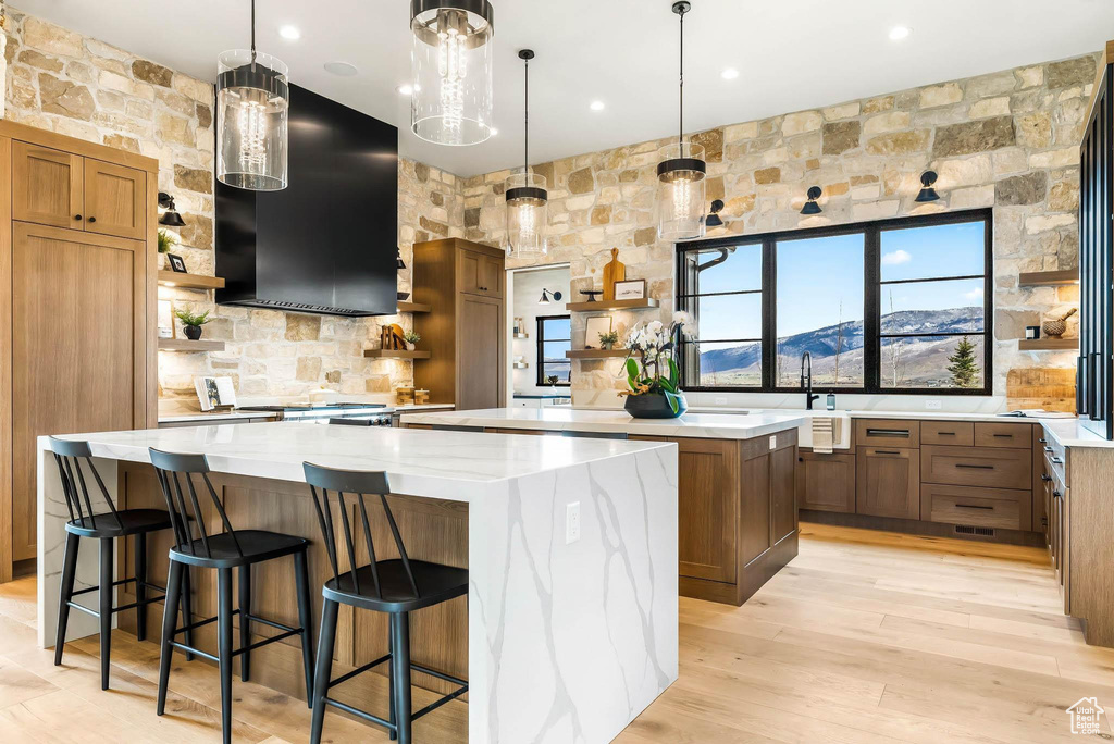 Kitchen with open shelves, a spacious island, range hood, light wood-type flooring, and recessed lighting