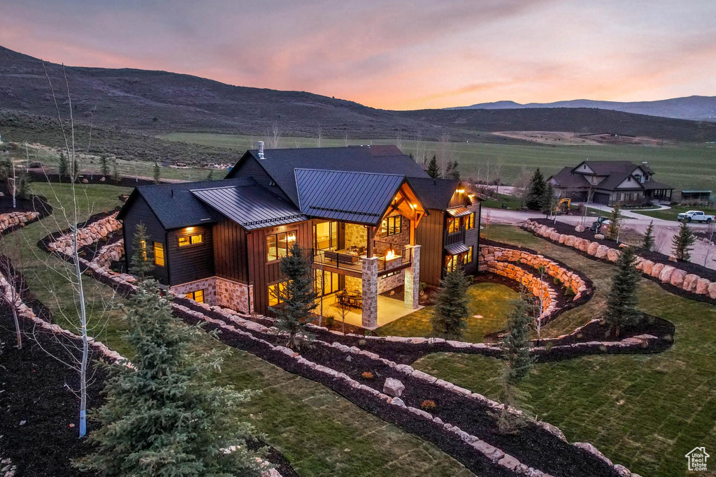 Rear view of house featuring a standing seam roof, a mountain view, stone siding, a metal roof, and a lawn
