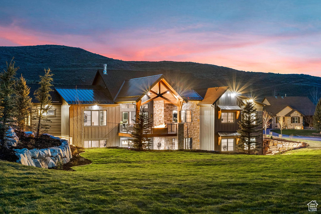 Back of property at dusk featuring stone siding, a standing seam roof, board and batten siding, and a lawn