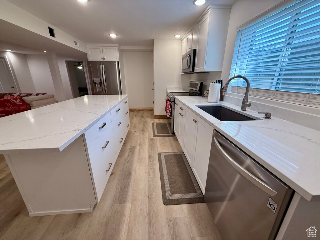 Kitchen featuring stainless steel appliances, a kitchen island, light wood-style flooring, light stone counters, and white cabinetry