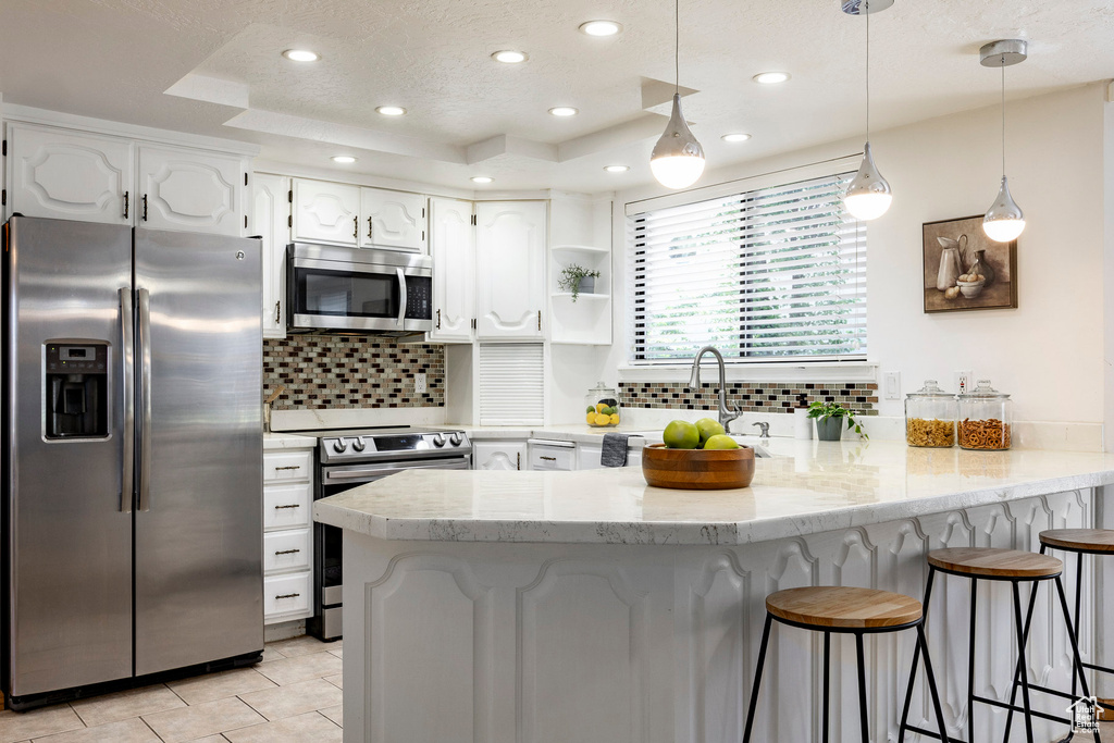 Kitchen featuring appliances with stainless steel finishes, a peninsula, white cabinetry, decorative backsplash, and a breakfast bar