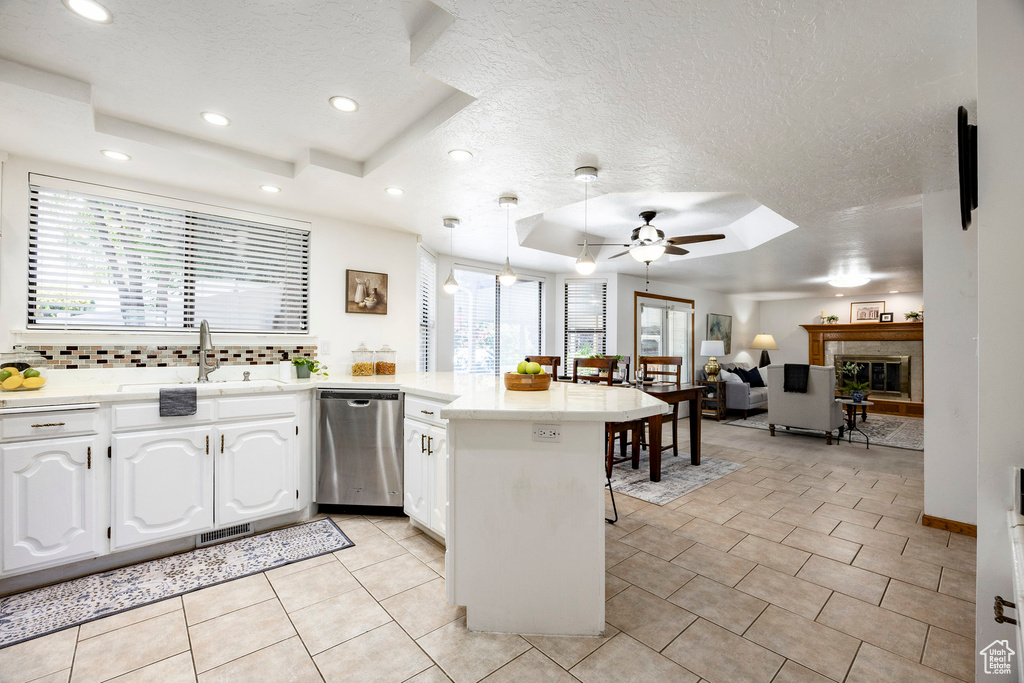 Kitchen with stainless steel dishwasher, a tray ceiling, a peninsula, ceiling fan, and a sink
