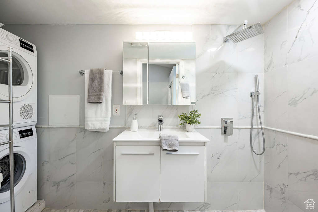 Full bathroom with stacked washing machine and dryer, vanity, a marble finish shower, and tile walls