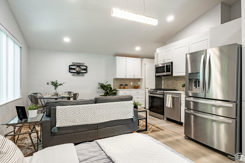 Kitchen featuring appliances with stainless steel finishes, decorative backsplash, vaulted ceiling, light wood-type flooring, and white cabinets