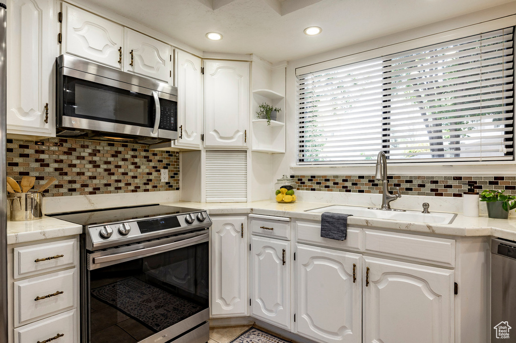 Kitchen with stainless steel appliances, a sink, white cabinetry, light tile patterned floors, and backsplash