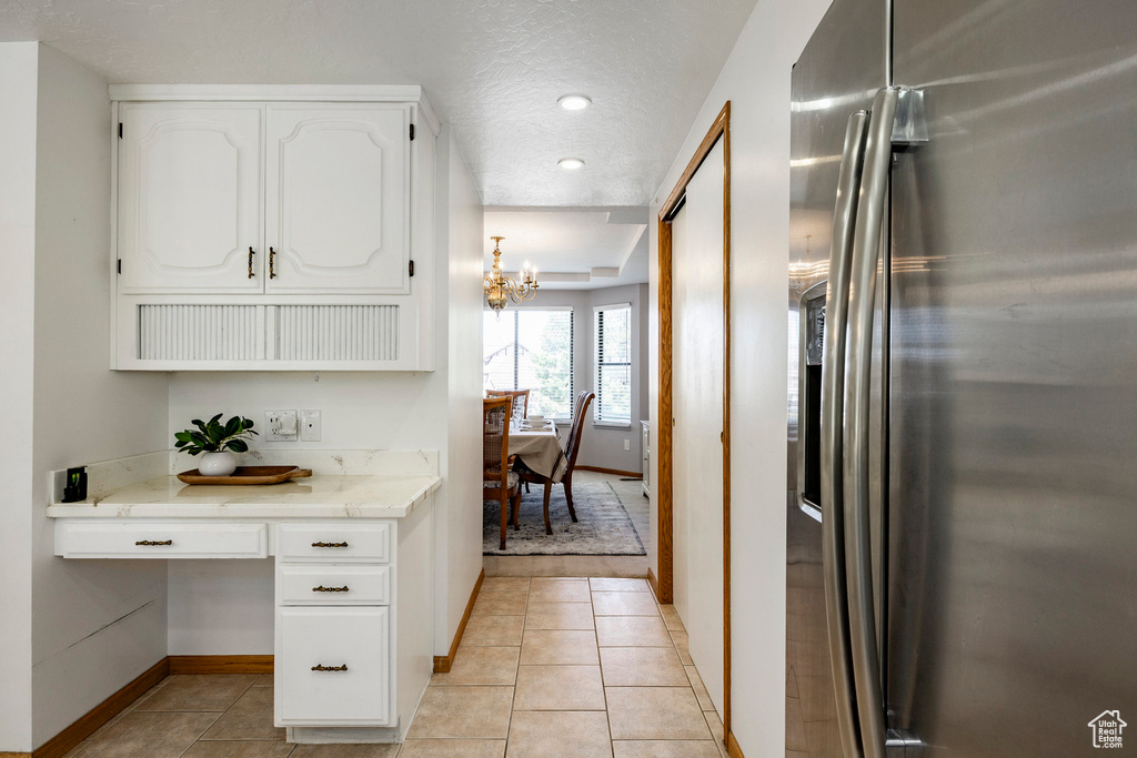 Kitchen with stainless steel fridge with ice dispenser, a chandelier, baseboards, white cabinetry, and light tile patterned floors