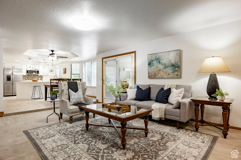 Living area featuring light carpet, a ceiling fan, baseboards, and a textured ceiling