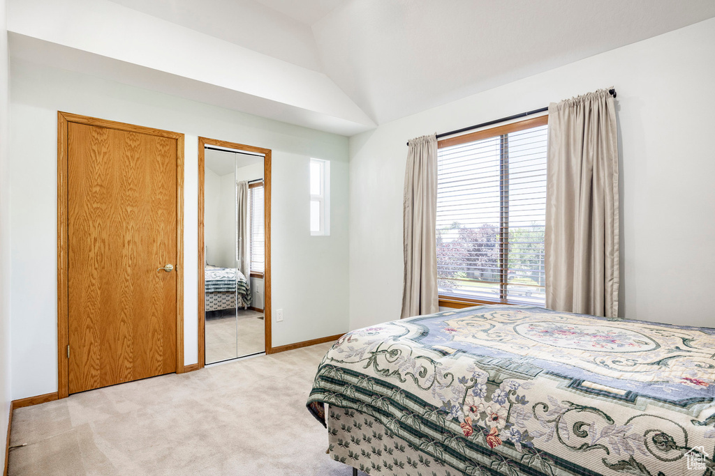 Bedroom featuring light carpet, vaulted ceiling, and baseboards