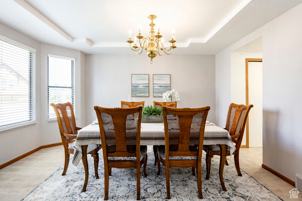 Dining area with a raised ceiling, a chandelier, and light carpet