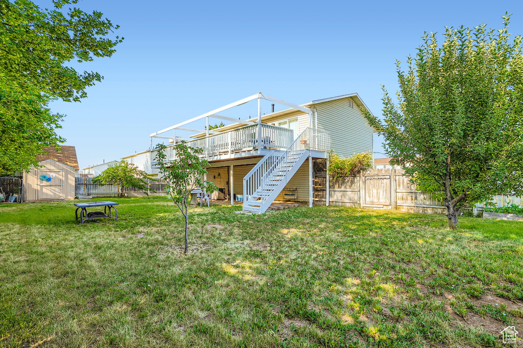 Rear view of property with stairway, a wooden deck, a storage unit, and a fenced backyard