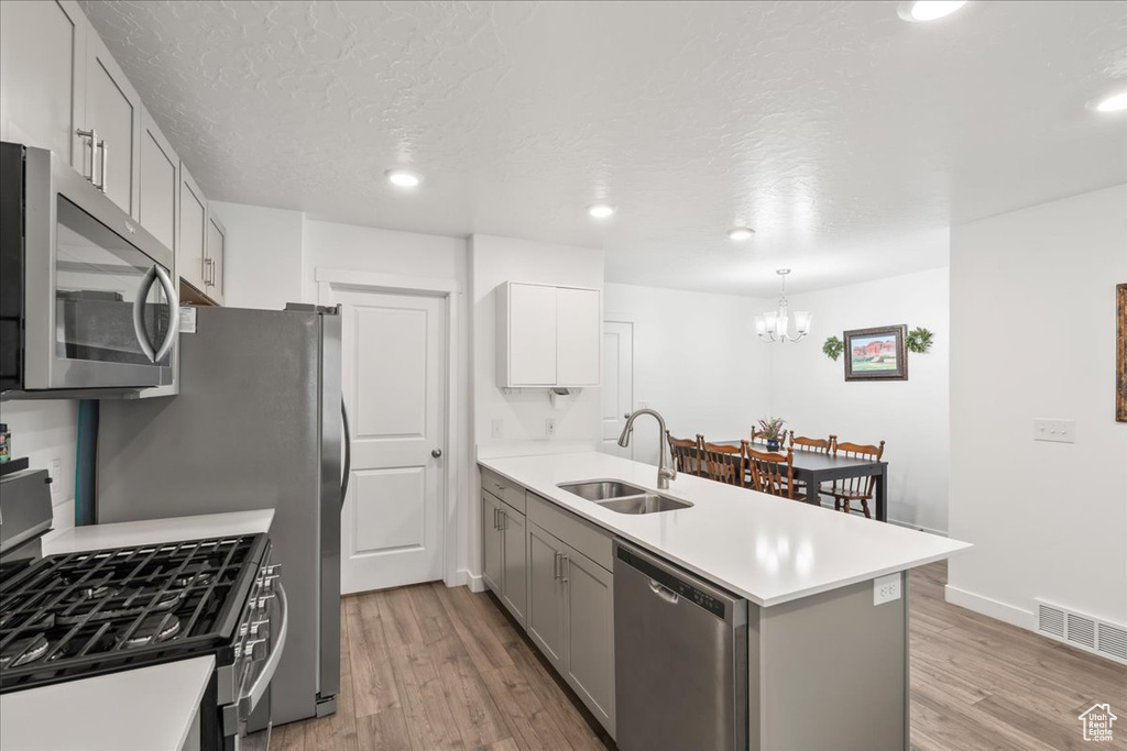 Kitchen with appliances with stainless steel finishes, a peninsula, light wood finished floors, a chandelier, and a textured ceiling