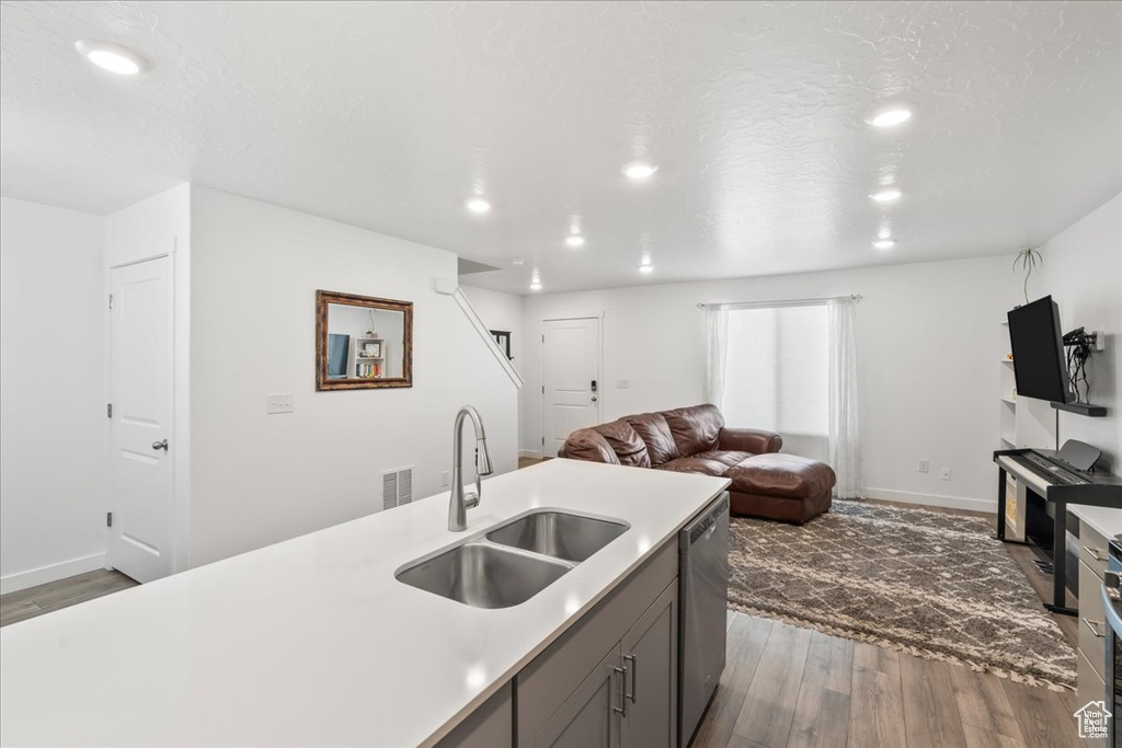 Kitchen with open floor plan, wood finished floors, light countertops, stainless steel dishwasher, and recessed lighting