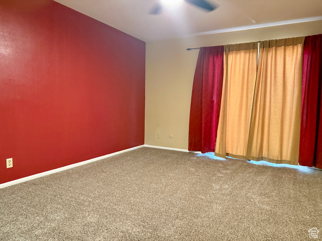 Carpeted empty room with a ceiling fan and baseboards