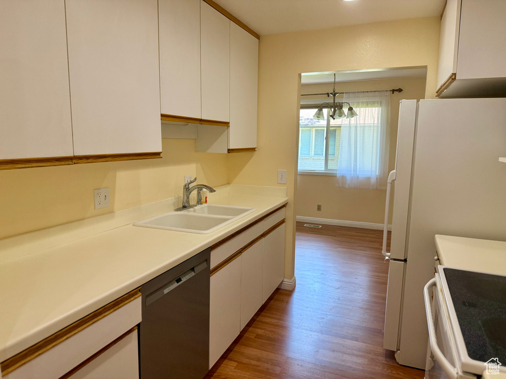 Kitchen with white appliances, white cabinets, wood finished floors, a chandelier, and light countertops