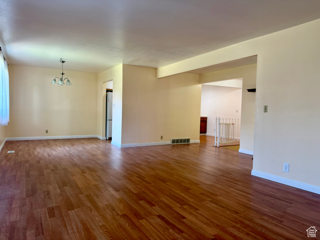 Unfurnished living room featuring a chandelier and dark wood-style flooring