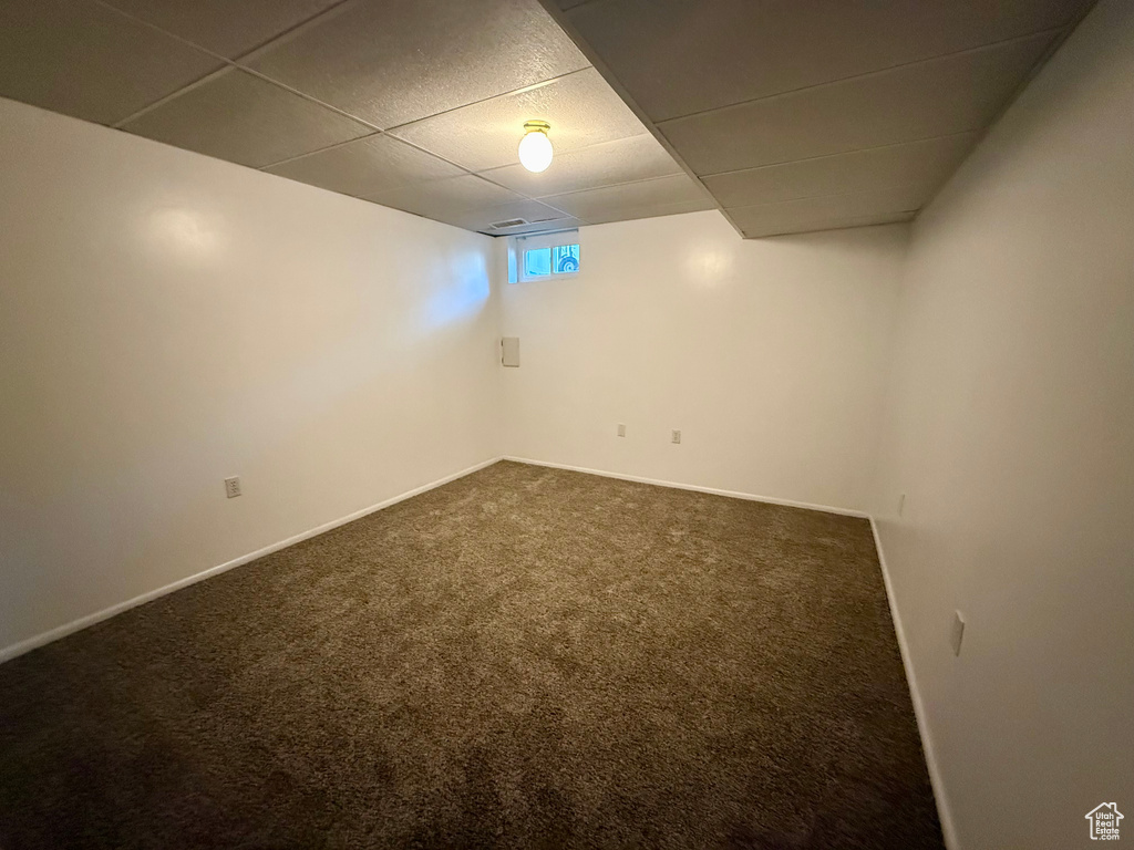 Below grade area with a paneled ceiling and dark colored carpet