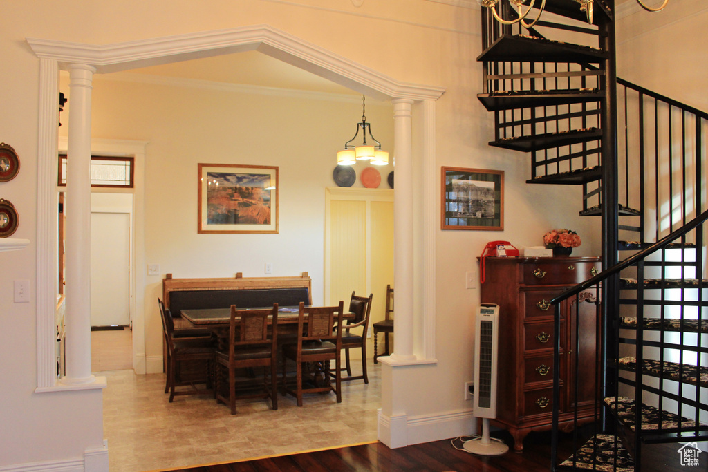 Dining area with wood finished floors, stairs, ornate columns, and crown molding