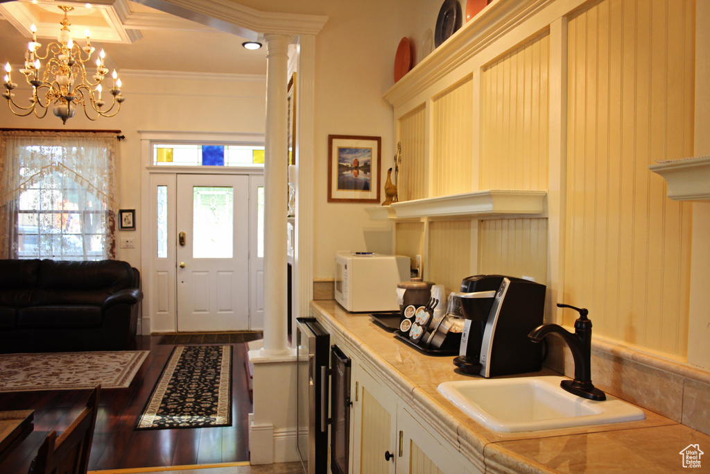 Entryway with beverage cooler, crown molding, a chandelier, and decorative columns