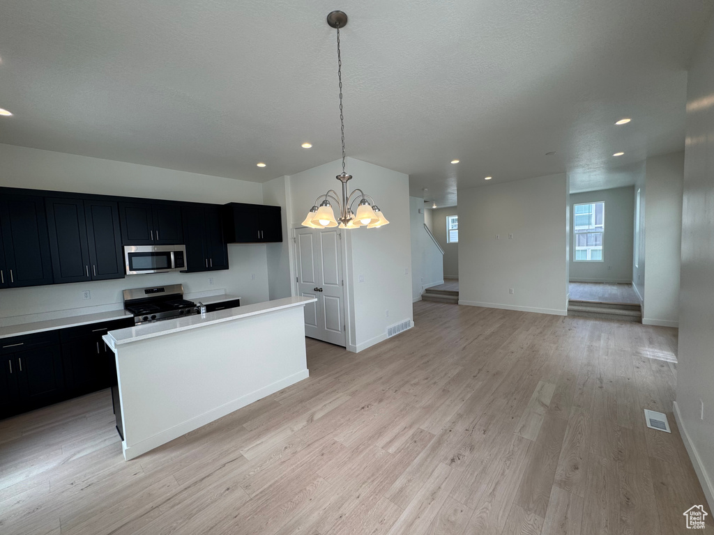 Kitchen with stainless steel appliances, dark cabinets, a chandelier, recessed lighting, and a center island with sink