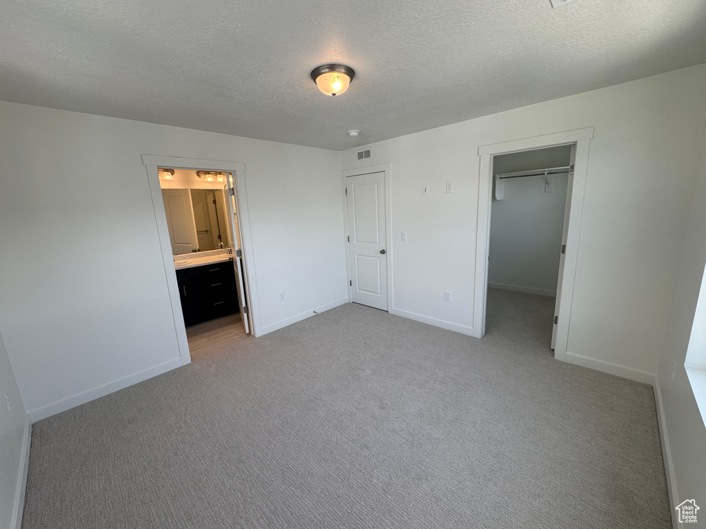 Unfurnished bedroom with carpet flooring, a textured ceiling, a walk in closet, ensuite bath, and a closet