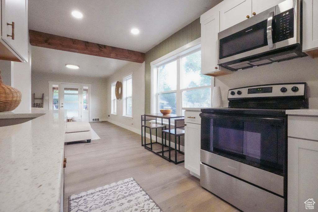 Kitchen with stainless steel appliances, beam ceiling, recessed lighting, light wood-style flooring, and white cabinetry