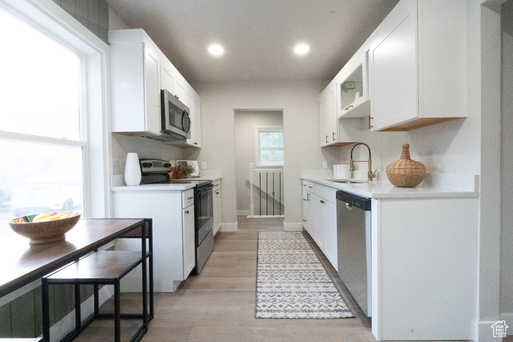 Kitchen with appliances with stainless steel finishes, white cabinets, light countertops, recessed lighting, and light wood-style flooring