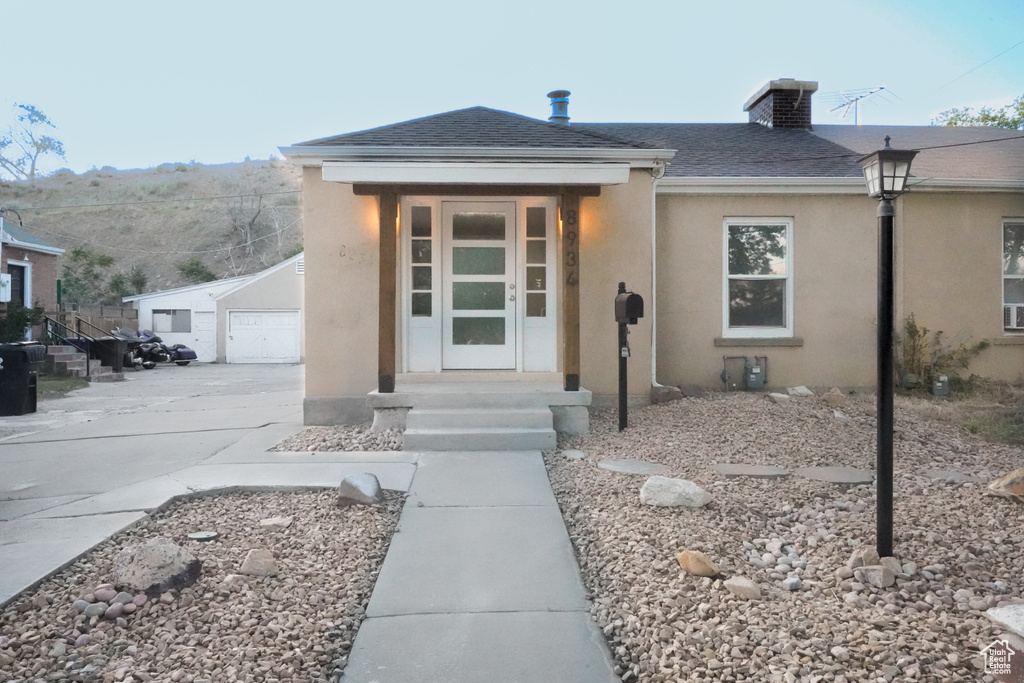 View of front facade featuring stucco siding, a detached garage, an outbuilding, a chimney, and roof with shingles