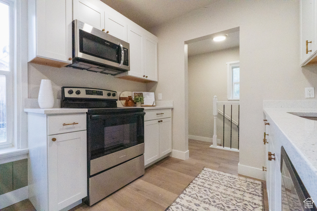 Kitchen featuring stainless steel appliances, light wood-style floors, white cabinets, and light countertops