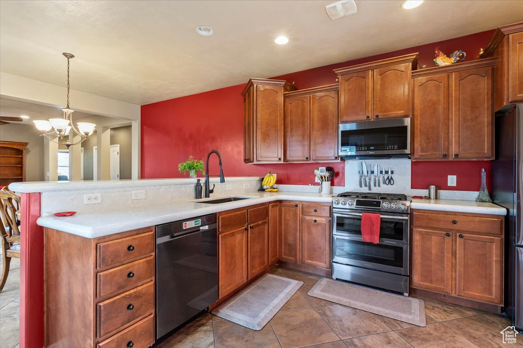 Kitchen featuring appliances with stainless steel finishes, a peninsula, light countertops, a chandelier, and brown cabinetry